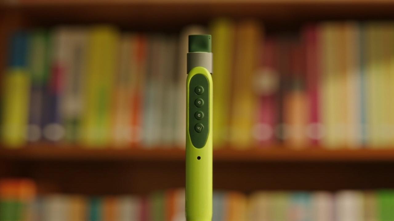 K7 reading pen in front of a bookshelf filled with colorful OID audio book series